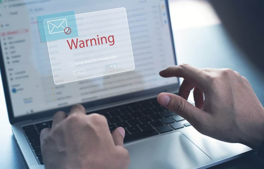 Blocking spam e-mail, warning pop-up for phishing mail, network security concept. Business man working on laptop computer at home with warning window on screen
