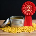 open tin of furniture polish with lid to the left 2nd place red ribbon to the right and tin surrounded by beeswax pellets