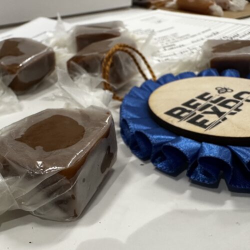 four wrapped pieces of caramels on a white round cardboard with blue 1st place ribbon to the right of picture