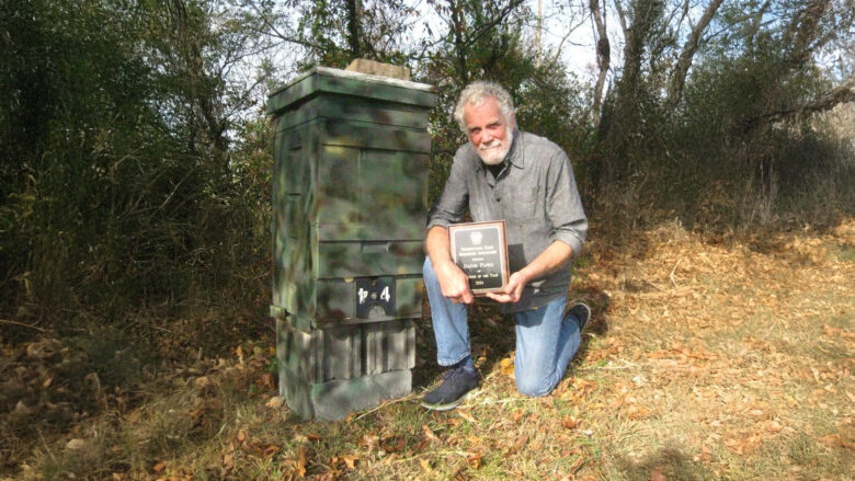 David Parker kneeling at beehive with citation